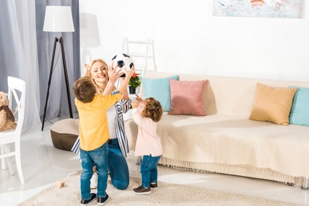 A mom playing soccer with her kids in the living room.